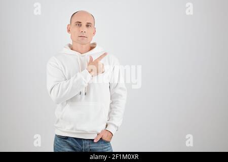 Portrait of handsome middle-aged an in white hoodie looking at camera and pointing away, isolated on white Stock Photo