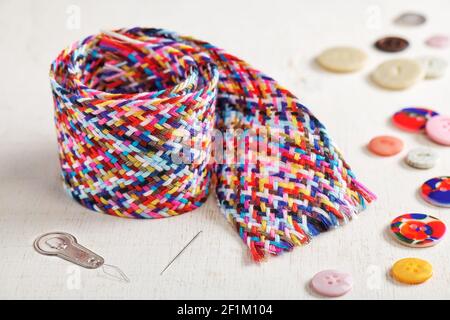 A braid of multi-colored sewing threads, needle, needle threader and buttons lying on a white surface Stock Photo