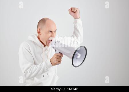 Angry mature man in white hoodie shouting in megaphone demanding justice Stock Photo