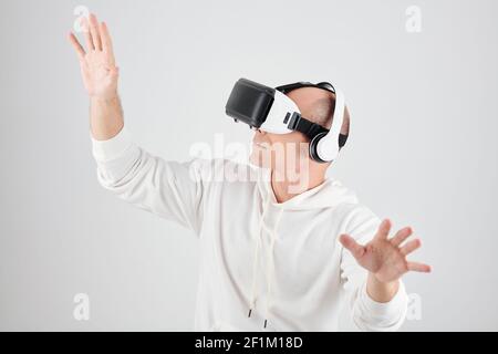 Serious mature man in white hoodie playing video game in virtual reality headset Stock Photo