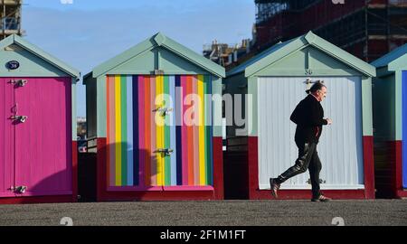 Brighton UK 9th March 2021 - A runner passes by colourful beach huts along Hove seafront on a beautiful sunny morning as wet and stormy weather is forecast to arrive in the next few days throughout Britain : Credit Simon Dack / Alamy Live News