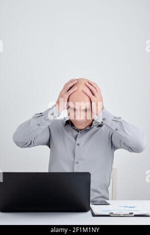 Frustrated stressed businessman clasping head when reading e-mail on laptop screen or accidenly deleting important document Stock Photo