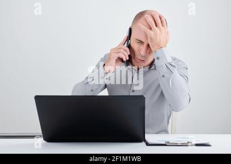 Businessman making face palm gesture when talking on phone with manager of failed project Stock Photo