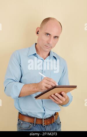 Portrait of serious middle-aged man writing or drawing on tablet computer with digital pen and looking at camera Stock Photo
