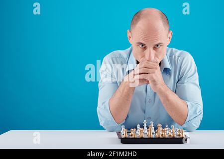 Portrait of serious middle-aged man sitting at table with chessboard and looking at camera pondering over game strategy Stock Photo