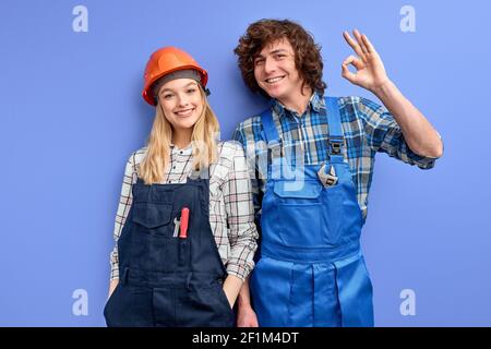 man and woman smiling civil engineers wearing uniform and hardhats working at industrial factory. Engineering and architecture concept. Man showing OK Stock Photo