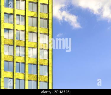 Facade of a yellow building with windows against a blue sky with clouds. Stock Photo