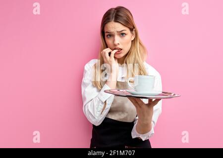 waitress woman holding tray with cup over isolated pink background stressed and worried. Fear and upset for mistake. portrait of young staff of restau Stock Photo