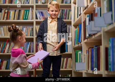 friendly children giving books to each other, help in library before school, smiling Stock Photo