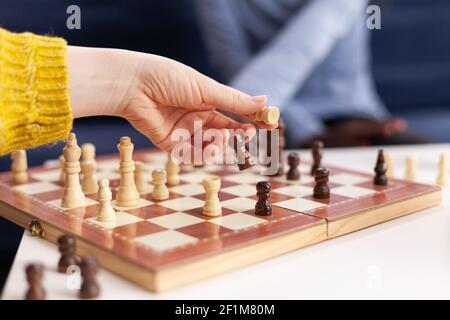 Close up of woman moving chess pieces on board during global pandemic with coronavirus. Group of friends having fun in home living room. Conceptual image. Board games, competing, tactics, asctivity. Stock Photo