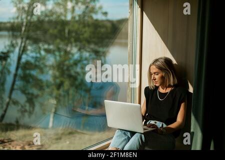 Woman using laptop near window Stock Photo
