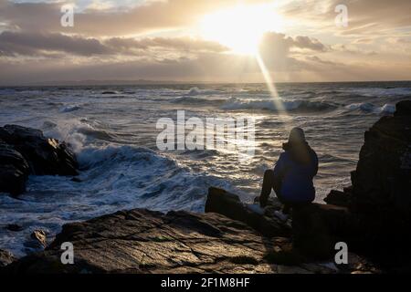 Woman sitting on rocks and looking at sea Stock Photo