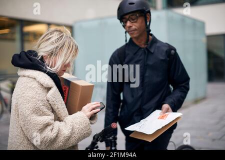 Bicycle courier taking sign from female customer while delivering package Stock Photo