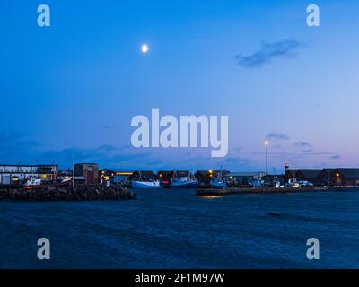 Moon in evening sky over harbor Stock Photo