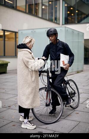 Bicycle courier taking sign from female customer while delivering package Stock Photo