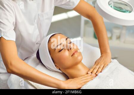Cosmetologist or masseur making facial massage with upper shoulder girdle for woman in beauty salon Stock Photo