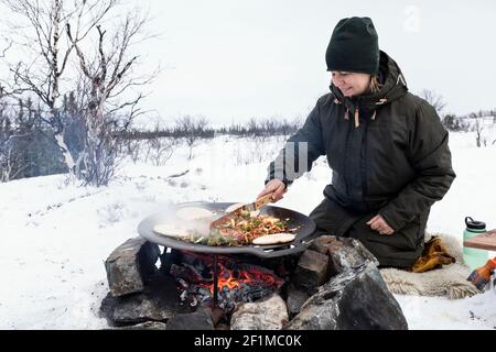 Woman preparing food over campfire Stock Photo