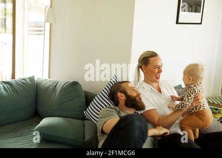 Parents playing with baby girl on sofa Stock Photo