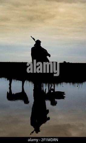 A wildfowler, or duck hunter, with his dog on a Lincolnshire salt marsh at last light by a pool with his dogs Stock Photo