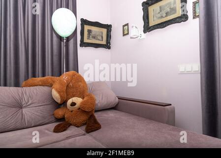 Handstanding stuffed toy with balloon. Funny Teddy bear turned upside down on sofa, falling over. People goes crazy in quarantine. Stock Photo