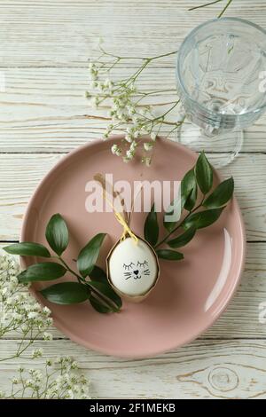 Happy Easter table setting with a cute egg bunny, greenery and gypsophila on a white wooden table Stock Photo