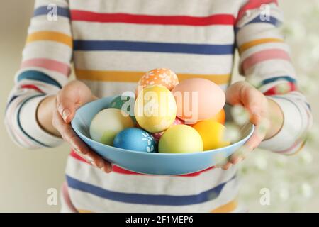 Child in a striped sweater holding a blue plate of colorful Easter eggs, family tradition close up Stock Photo