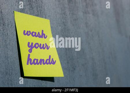 3D rendered protective memo sticker against Covid-19 and coronavirus on wooden texture concept: Yellow paper with reminder message WASH YOUR HANDS Stock Photo