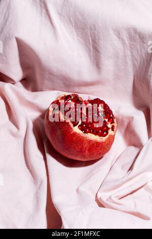 One red pomegranate on pink textile background. Modern fruit still life Stock Photo