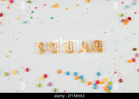Word sugar made of cookie letters and rainbow sprinkles on white background, view from the top Stock Photo