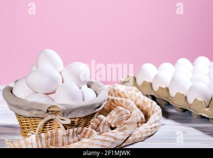 White Chicken eggs in a cardboard box and in a Straw basket on a pink background with piece of cloth, Raw Fresh Chicken Eggs in a paper container Stock Photo