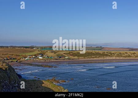 Lines of waves running in towards the sandy beach at Corbie Knowe at the southern end of Lunan Bay with Farm Polytunnels on the Fields above the Commu Stock Photo