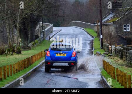 Vauxhall Mokka car travelling on rural road through puddle (splashing spraying surface water) on wet rainy day - Bolton Bridge, Yorkshire, England, UK Stock Photo