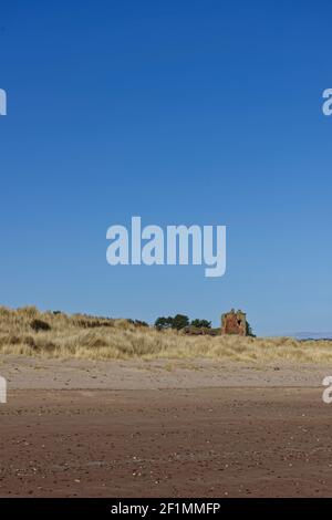 The Keep of the Red Castle Ruins just visible above the low Grass covered Dunes of Lunan Bay near to Lunan water on a bright March Morning. Stock Photo