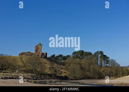 The leaning Keep of Red Castle built on a grass covered mound overlooking the mouth of Lunan Water, and old Tank trap Blocks in the River. Stock Photo