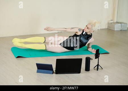 Fit young woman in leather lotard and knee high socks doing side-lying leg lifts when filming herself for blog Stock Photo