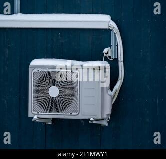 Heat pump mounted on the wall of a house and covered in snow. Stock Photo