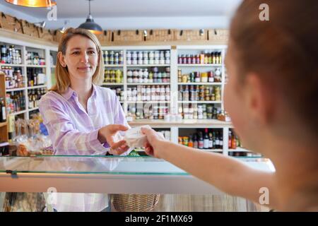 Female Customer Delicatessen Food Store Buying Local Cheese From Sales Assistant Stock Photo