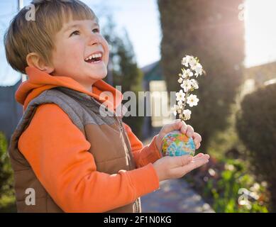 cute laughing boy of 4 years old holds small ball - globe from which spring blossoming apricot branch sticks out in bright backlight. Eco concept, env Stock Photo
