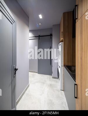 Modern interior of empty laundry room in luxury private house. Grey tones. Wooden cabinets. Washing machine. Stock Photo