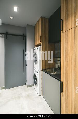 Modern interior of empty laundry room in luxury private house. Grey tones. Wooden cabinets. Washing machine. Stock Photo