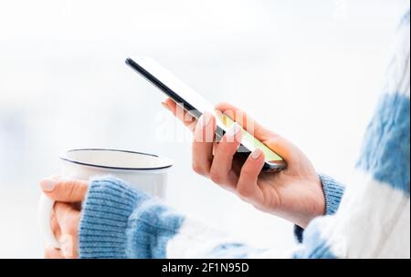 Hands holding white cup and using phone Stock Photo