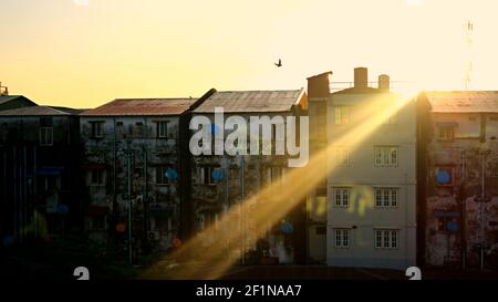 Good Morning Yangon: Sunbeam on rooftop of low rise buildings with a silhouette of a sole flying bird as the sun rises in the city capital of Myanmar Stock Photo
