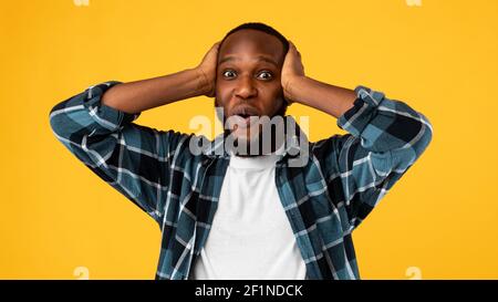 Omg. Surprised African American Guy Touching Head Looking At Camera In Amazement And Shock Posing Standing Over Yellow Studio Background. Wow News Con Stock Photo