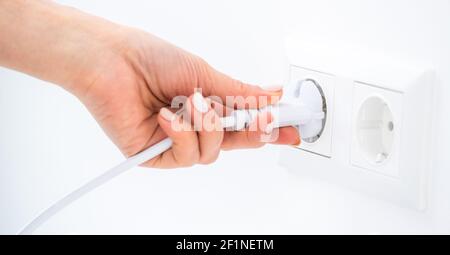 Hand plugging wire into socket on white wall Stock Photo