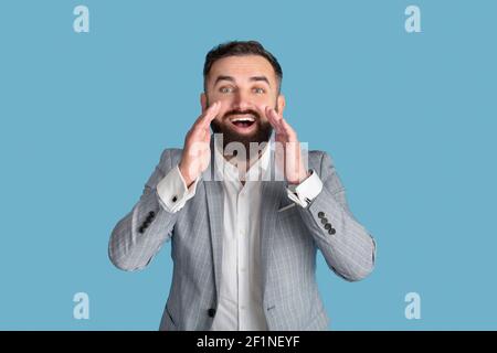 Excited young office manager shouting with hands near his mouth over blue studio background. Happy millennial businessman making announcement, adverti Stock Photo