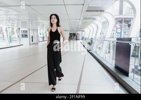 Young attractive Asian woman wearing black, is walking towards the camera in an elegant city walkway, Bangkok Thailand. Stock Photo