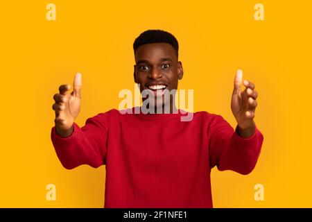 Come To Me. Excited Black Guy Extending Hands At Camera, Holding Big Invisible Oblect, African Man Offering Hugs Or Wants To Grab Something, Standing Stock Photo