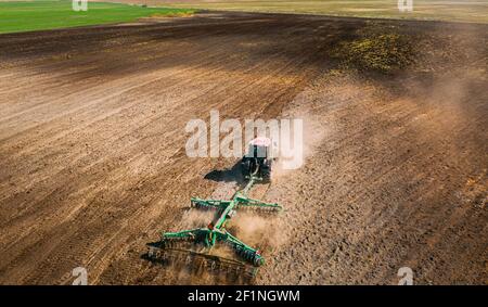 Aerial View. Tractor Plowing Field. Beginning Of Agricultural Spring Season. Cultivator Pulled By A Tractor In Countryside Rural Field Landscape. Dust Stock Photo