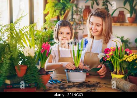 Cute child girl helps her mother to care for plants. Mom and her daughter engaged in gardening. Happy family in spring day. Stock Photo