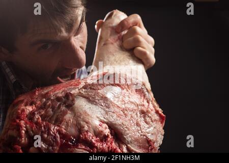 Crazy butcher eating fresh raw meat on black with copy space. Stock Photo